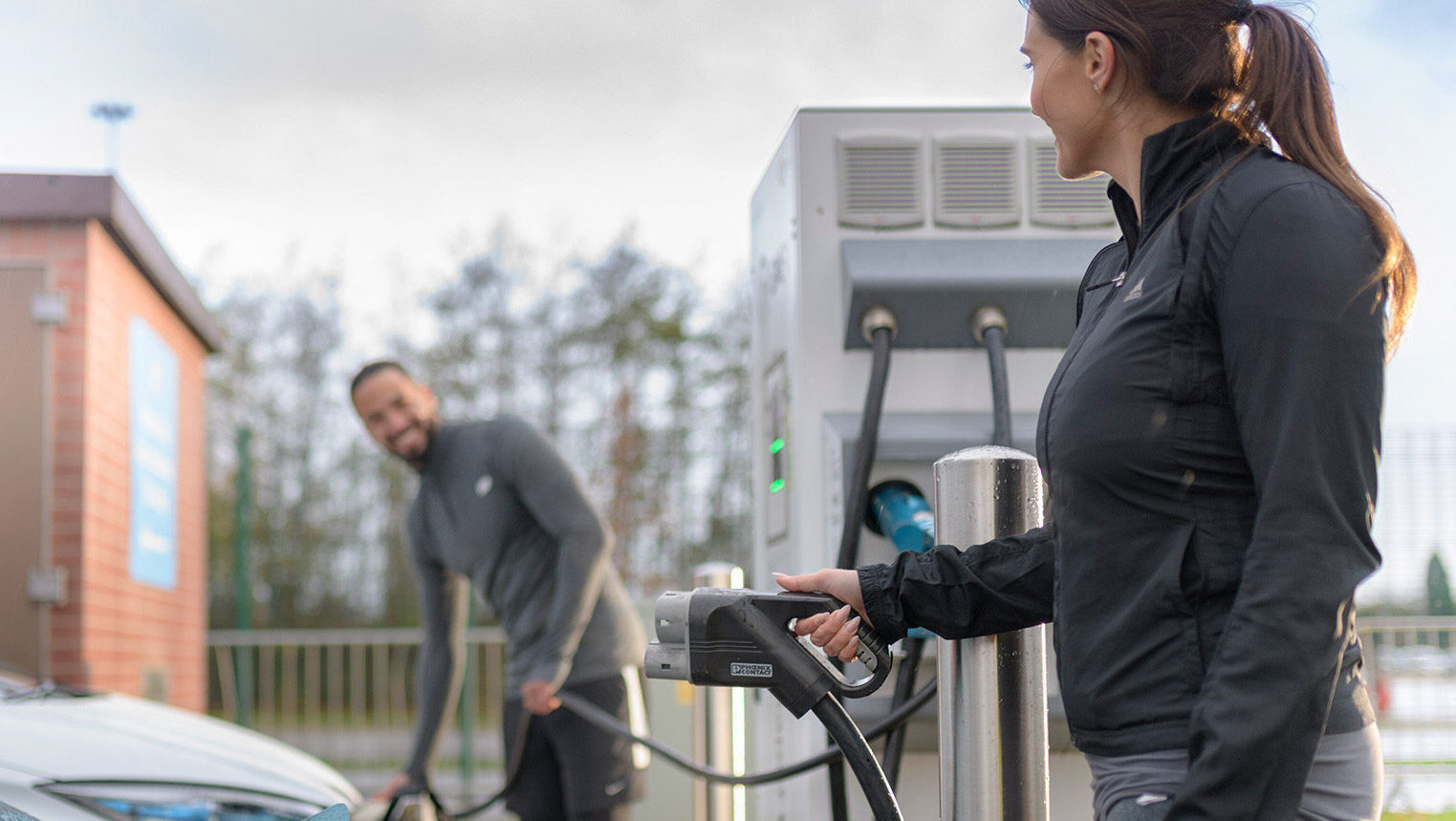 One man and one woman at a public charging station, both of them about to charge their parked cars