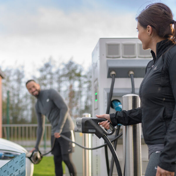 One man and one woman at a public charging station, both of them about to charge their parked cars