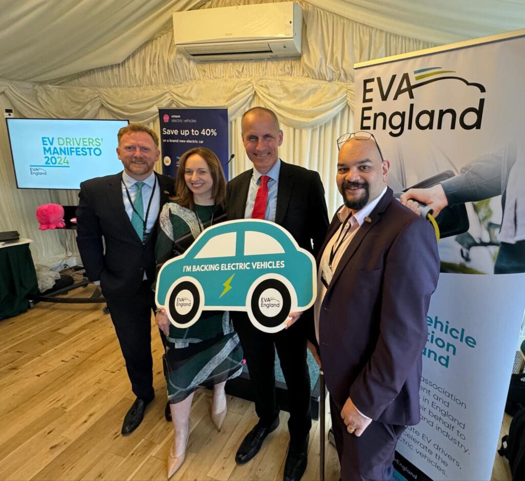 James Court, Fiona Howarth, Bill Esterson MP, and Warren Philips, standing in the Thames Pavilion by an EVA England banner, holding a car-shaped sign that says "I'm backing Electric Vehicles".